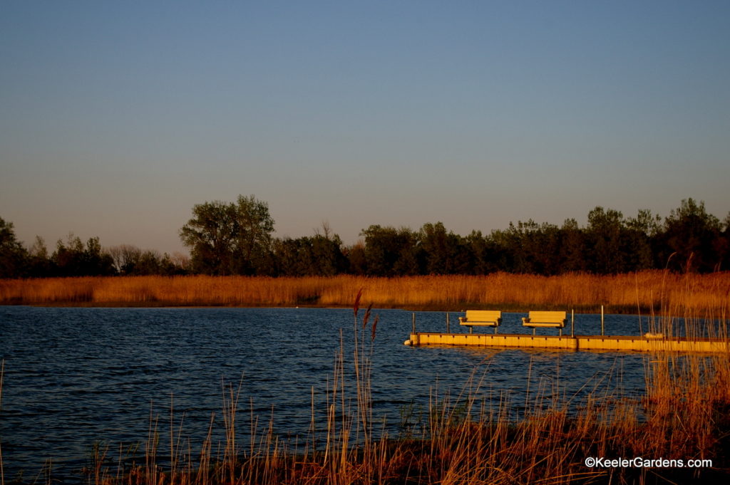 Two benchs positioned perfectly at the end of the dock are drenched with the orange tones of sunset looking southward on Saginaw Bay on Lake Huron in northern Michigan.